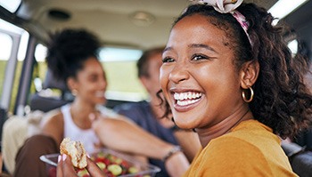 Woman smiling while eating meal with friends in car