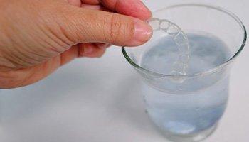 a person putting nightguards in a glass of water