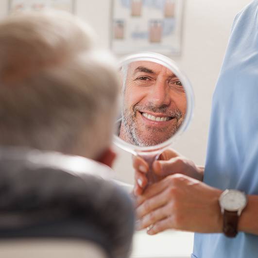 Man looking at smile in mirror after metal free dental restorations