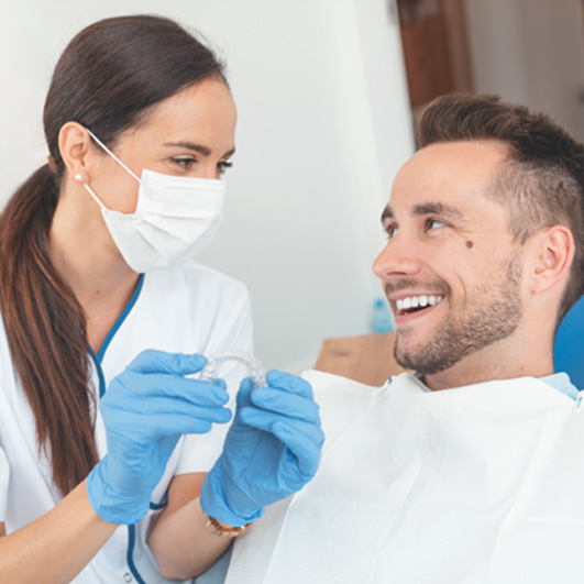 Patient smiling at dentist holding clear aligner