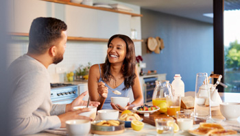 Couple smiling at each other while eating in kitchen