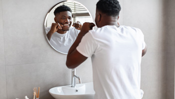 Man smiling while flossing in bathroom