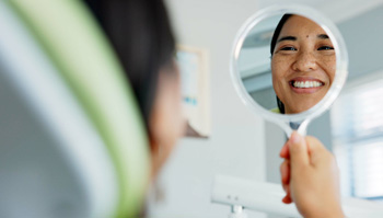 Woman smiling at reflection in handheld mirror
