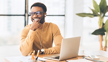 a smiling person with headphones in working on their laptop