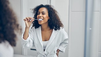woman in a white bathrobe brushing her teeth in front of a mirror 