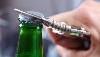person opening a green glass bottle with a bottle opener 