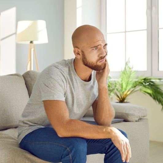 Frowning man sitting on sofa, suffering from mouth pain