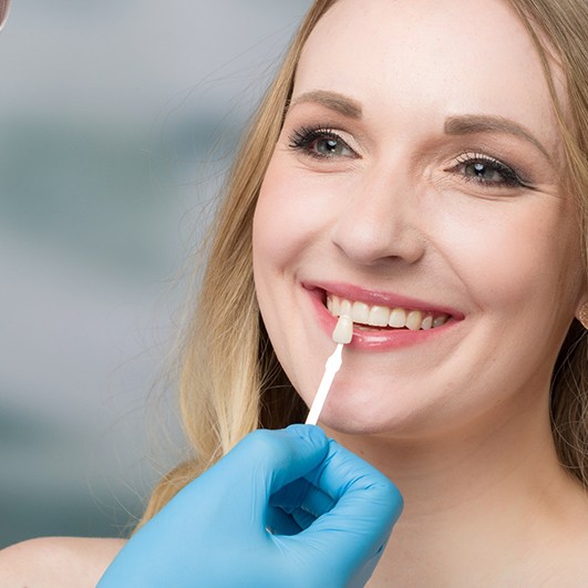 A dentist using a shade guide to determine the correct color for this female patient’s new veneers