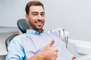 Bearded man giving thumbs up in dental chair